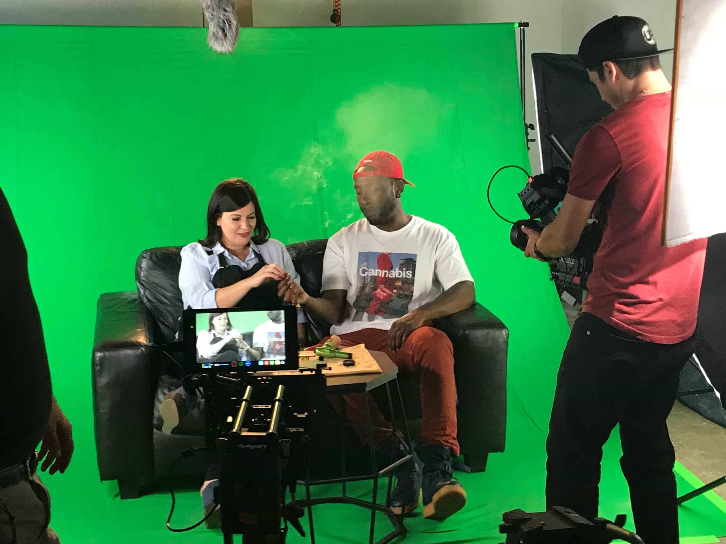 Two people sitting on a couch in front of a green screen filming a video.