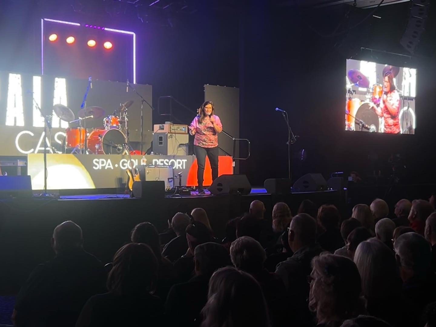 A man speaks on stage at a crowded event with a screen behind him.