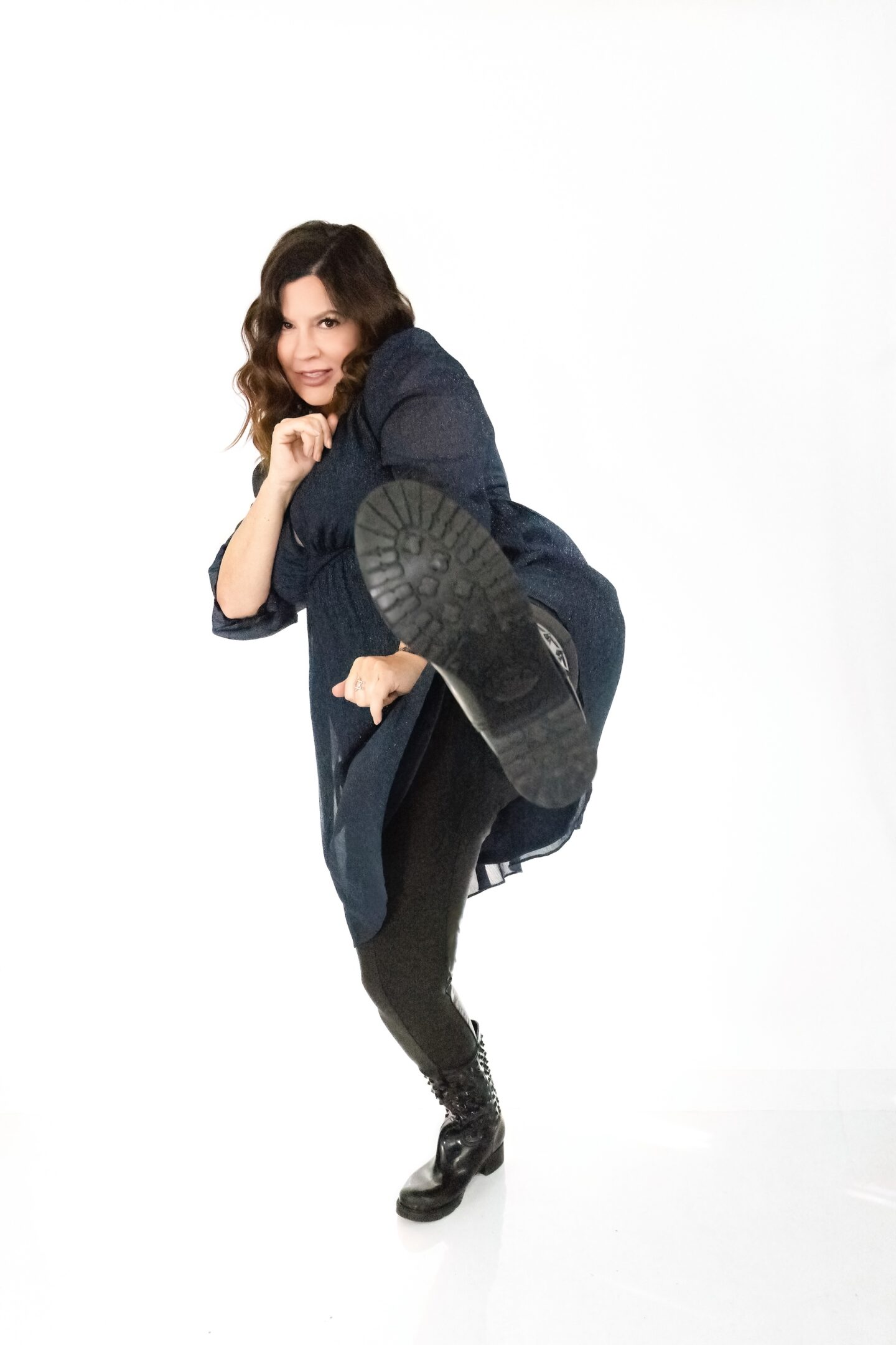 Confident woman kicking forward in casual dark outfit against white background.