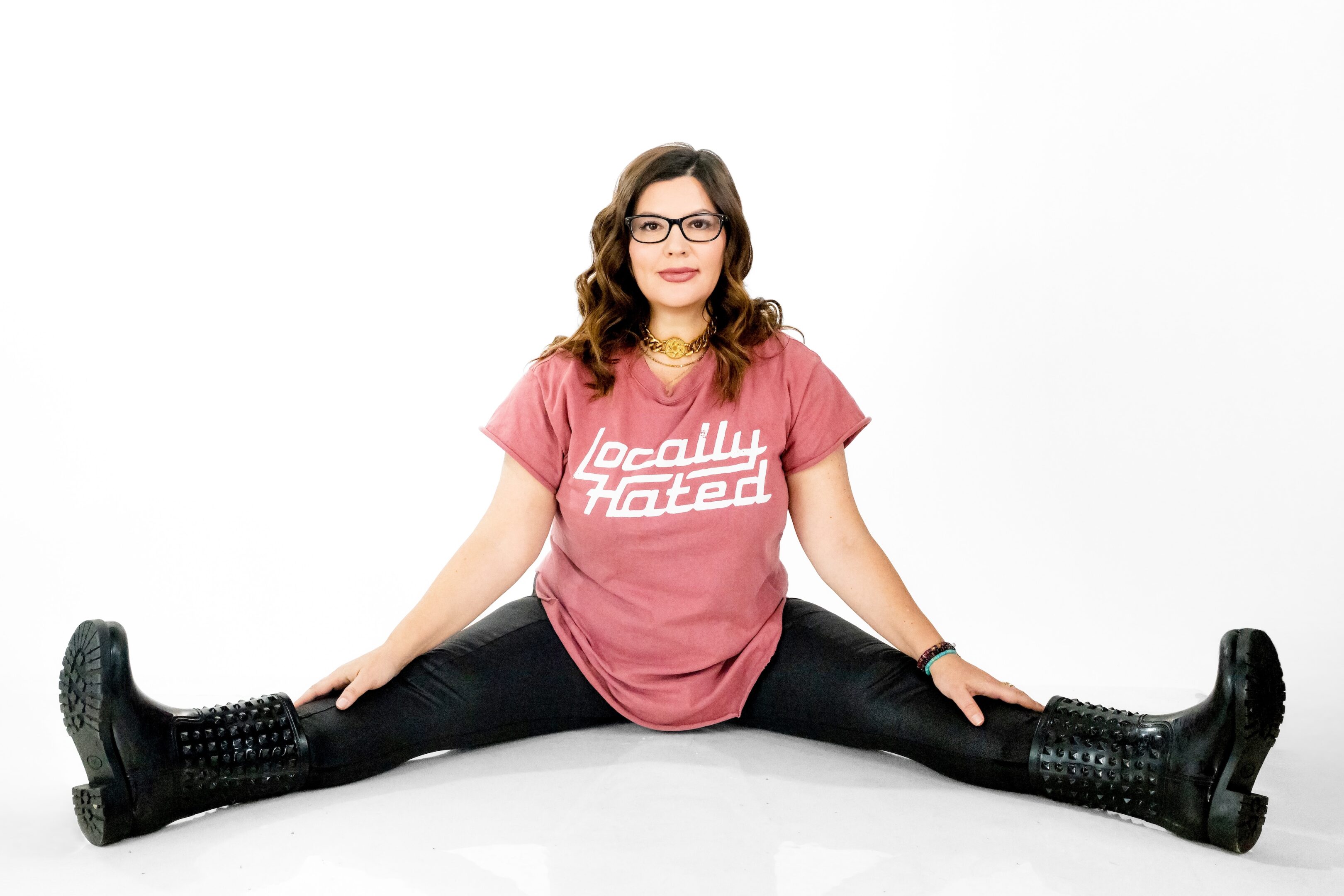 Woman in glasses doing a split, wearing a pink shirt and black pants.